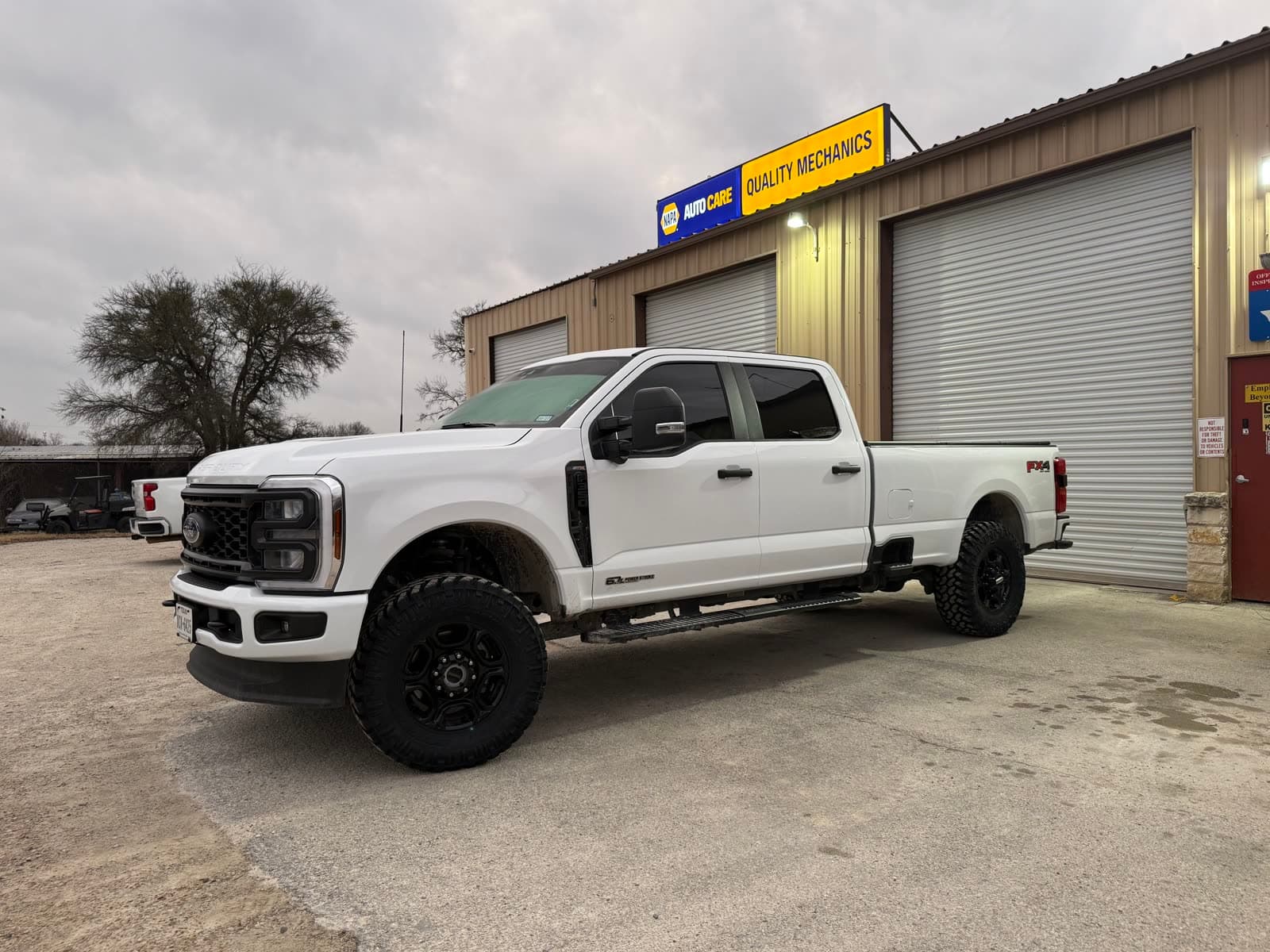 Lifted Ford F-250 parked in front of the Quality Mechanics shop and NAPA AutoCare sign on Gholson Road in Waco
